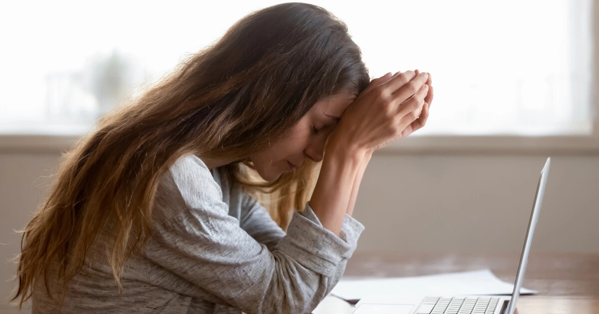 A woman in front of her laptop stressed with her hands in her head.